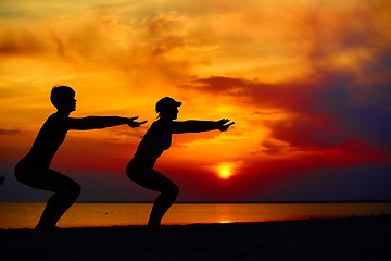 Image showing Yoga people training and meditating in warrior pose outside by beach at sunrise or sunset.