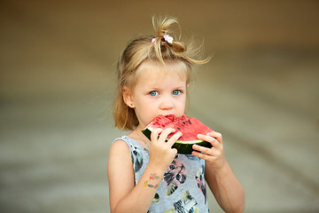 Image showing Adorable blonde girl eats a slice of watermelon outdoors.