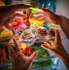 Image showing Human hands reaching for sweet cake at night in the open refrige