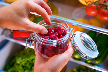 Image showing Woman takes the fresh raspberries from the open refrigerator