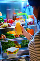 Image showing Woman takes the Orange juice from the open refrigerator