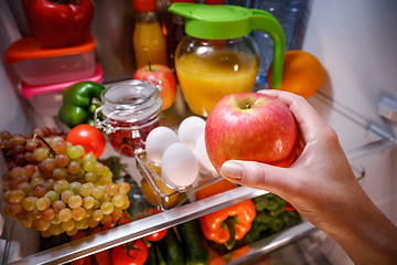 Image showing Woman takes the apple from the open refrigerator.