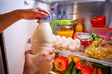 Image showing Woman takes the milk from the open refrigerator