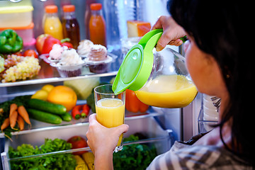 Image showing Woman takes the Orange juice from the open refrigerator