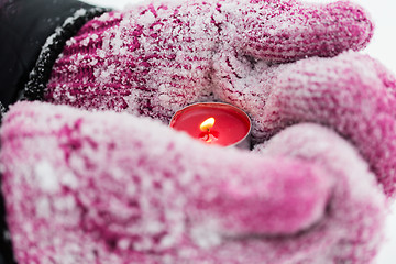 Image showing close up of hands in winter mittens holding candle