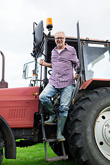 Image showing old man or farmer getting out of tractor at farm