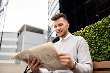 Image showing smiling man reading newspaper on city street bench