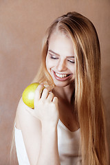 Image showing young pretty blond woman with green apple happy cheerful smiling close up on warm brown background, lifestyle people concept