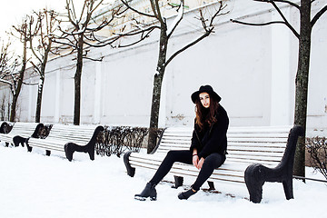 Image showing young pretty modern hipster girl waiting on bench at winter snow park alone, lifestyle people concept