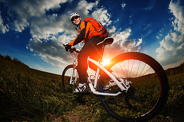 Image showing biker in orange jersey riding on green summer field