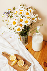 Image showing Simply stylish wooden kitchen with bottle of milk and glass on table, summer flowers camomile, healthy foog moring concept