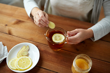 Image showing close up of woman adding ginger to tea with lemon