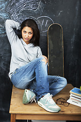 Image showing young cute teenage girl in classroom at blackboard seating on ta