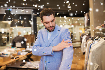 Image showing happy young man trying jacket on in clothing store