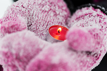 Image showing close up of hands in winter mittens holding candle