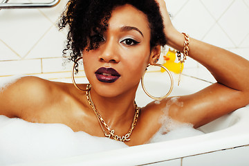 Image showing young afro-american teen girl laying in bath with foam, wearing swag jewelry flawless, making selfie, modern lifestyle concept