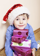 Image showing little cute boy with Christmas gifts at home. close up emotional face on boxes in santas red hat