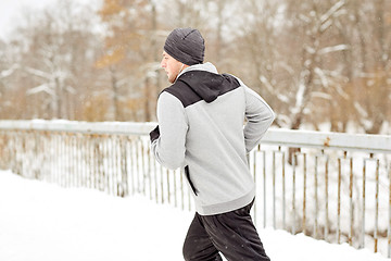 Image showing man in earphones running along winter bridge