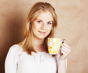 Image showing young cute blond girl drinking coffee close up on warm brown bac