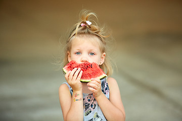 Image showing Adorable blonde girl eats a slice of watermelon outdoors.