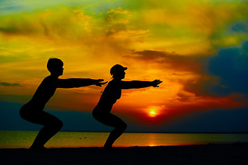 Image showing Yoga people training and meditating in warrior pose outside by beach at sunrise or sunset.