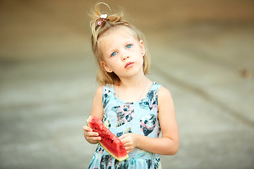 Image showing Adorable blonde girl eats a slice of watermelon outdoors.