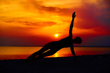 Image showing Silhouette of woman standing at yoga pose on the beach during an amazing sunset