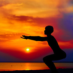 Image showing Silhouette of woman standing at yoga pose on the beach during an amazing sunset