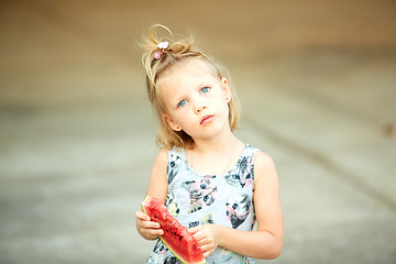 Image showing Adorable blonde girl eats a slice of watermelon outdoors.