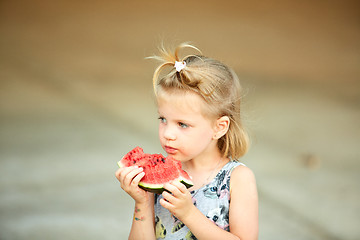 Image showing Adorable blonde girl eats a slice of watermelon outdoors.