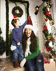 Image showing happy family on Christmas in red santas hats waiting gests and smiling infront of decorated house, mother and son, lifestyle people concept