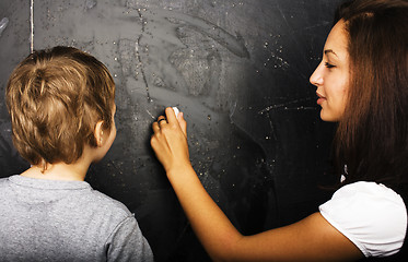 Image showing little cute boy with young teacher in classroom studying at blackboard, lifestyle education people concept