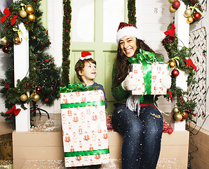 Image showing happy family on Christmas in red santas hats waiting gests and smiling infront of decorated house, mother and son, lifestyle people concept