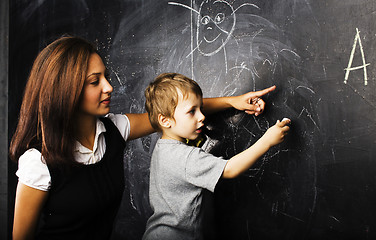 Image showing little cute boy with young teacher in classroom studying at blackboard, lifestyle education people concept