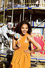 Image showing cool real teenage girl with candy near carousels at amusement pa