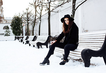 Image showing young pretty modern hipster girl waiting on bench at winter snow park alone, lifestyle people concept