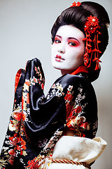 Image showing young pretty geisha in black kimono among sakura, asian ethno