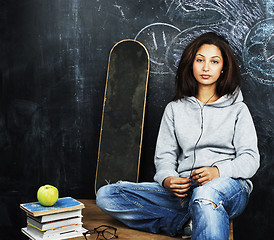 Image showing young cute teenage girl in classroom at blackboard seating on ta