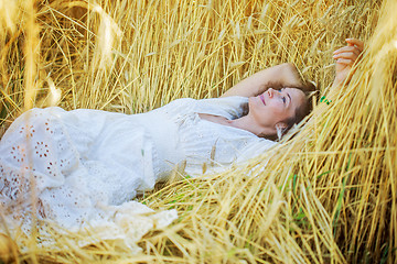 Image showing smiling woman in white dress lying among the ears of wheat