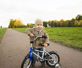 Image showing little cute real boy on bicycle emotional smiling close up outside in green amusement park