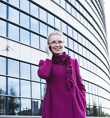 Image showing portrait of pretty young business woman in glasses talking on phone near modern building, lifestyle people concept