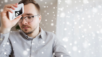 Image showing sad man with smartphone at home over snow