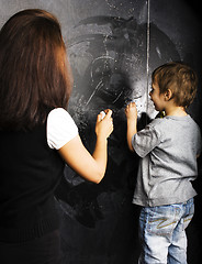 Image showing little cute boy with young teacher in classroom studying at blac