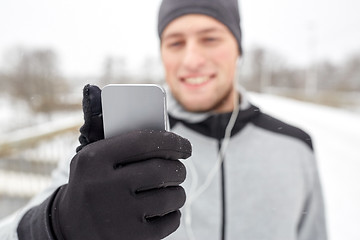 Image showing happy man with earphones and smartphone in winter