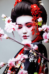 Image showing young pretty geisha in black kimono among sakura, asian ethno