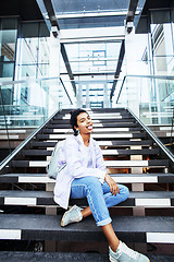 Image showing young cute modern indian girl at university building sitting on stairs reading a book, wearing hipster glasses, lifestyle people concept