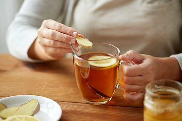 Image showing close up of woman adding ginger to tea with lemon