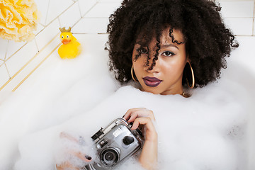 Image showing young afro-american teen girl laying in bath with foam, wearing swag jewelry flawless, making selfie