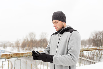 Image showing man in earphones with smartphone on winter bridge