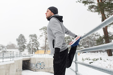 Image showing sports man stretching leg at fence in winter